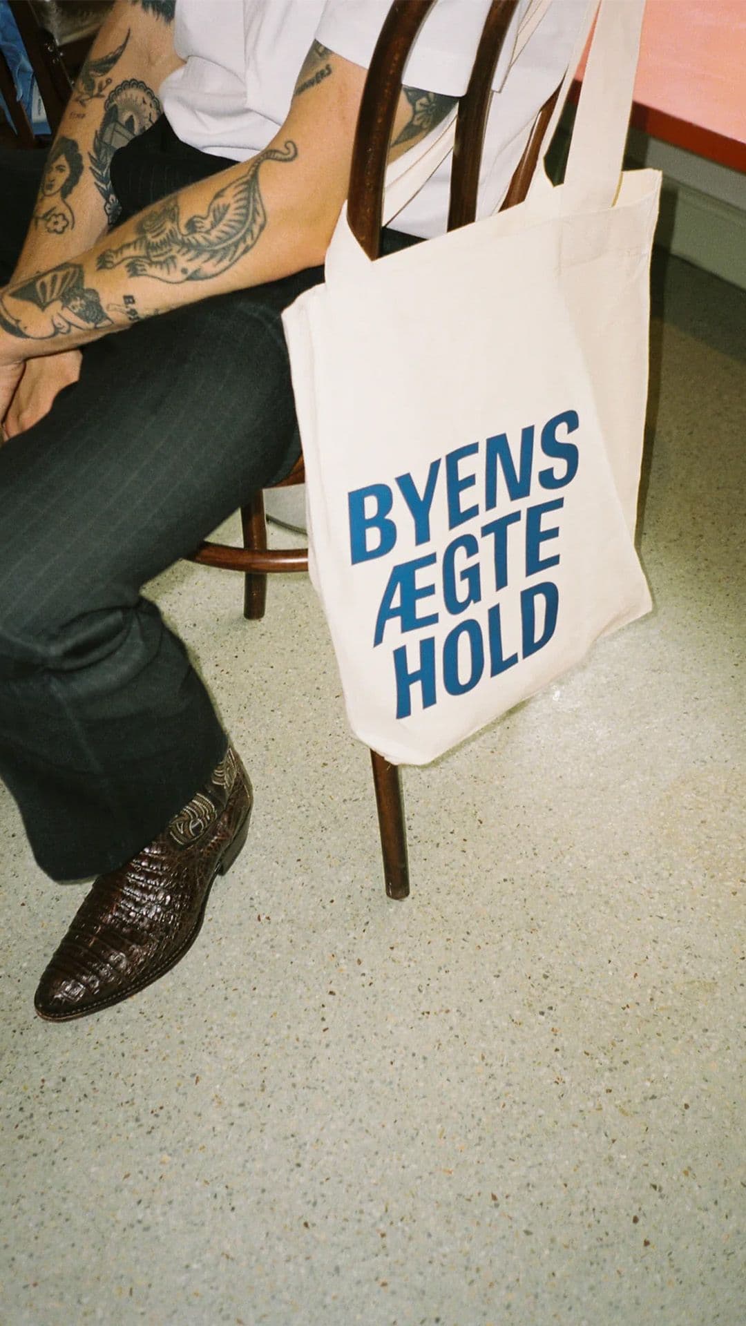 a person sitting in a chair with a tote bag that says byens ægte hold