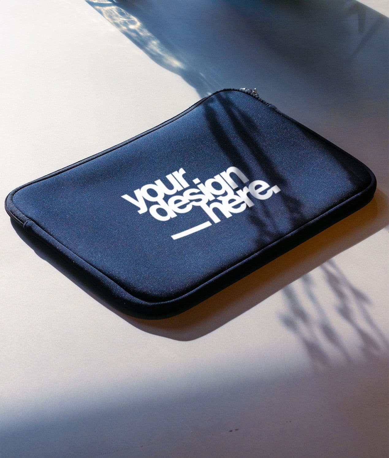 Dark blue laptop sleeve with "your design here." text on a light surface.