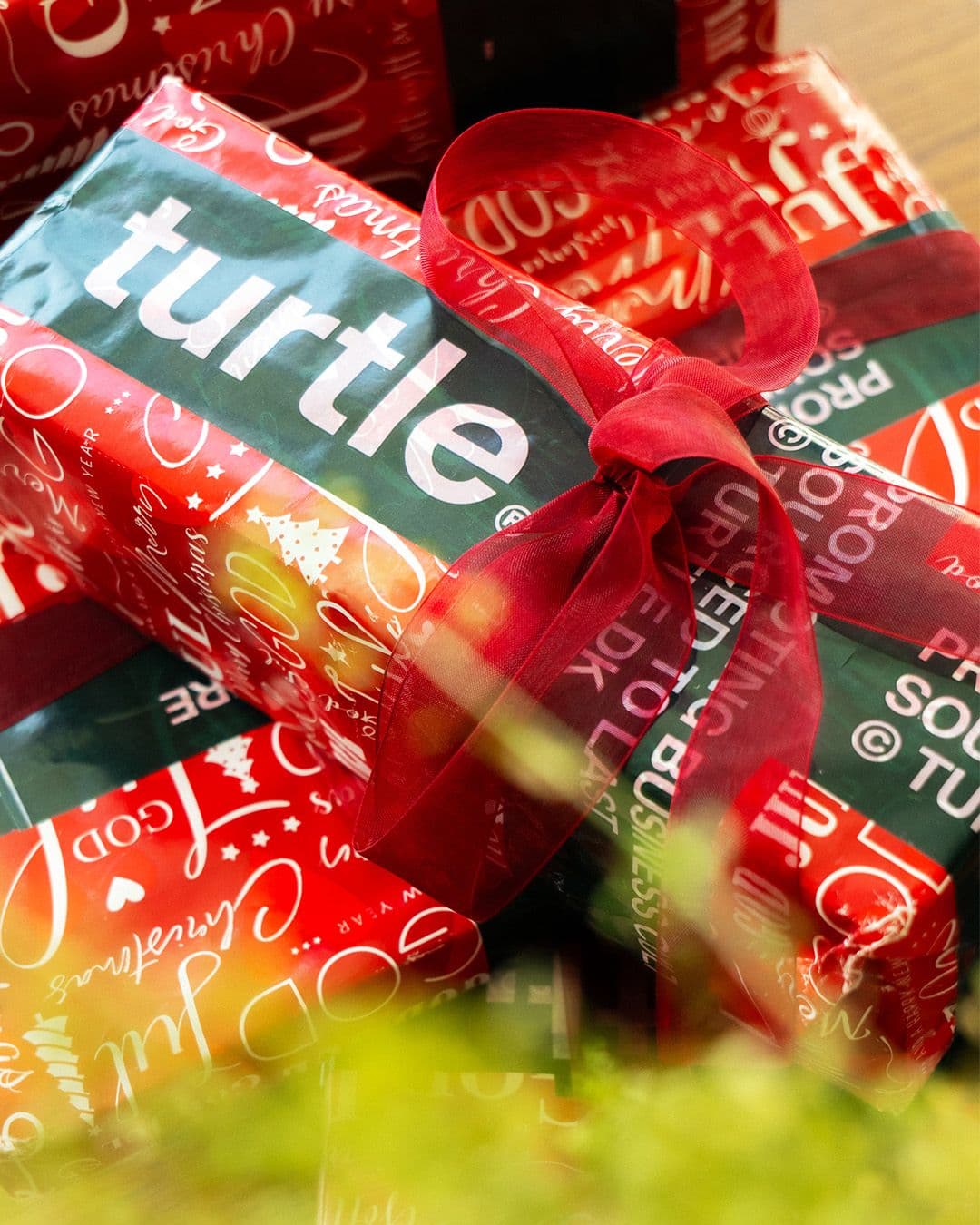 A stack of red and green Christmas gifts, one with "turtle" in white text, tied with a red bow.